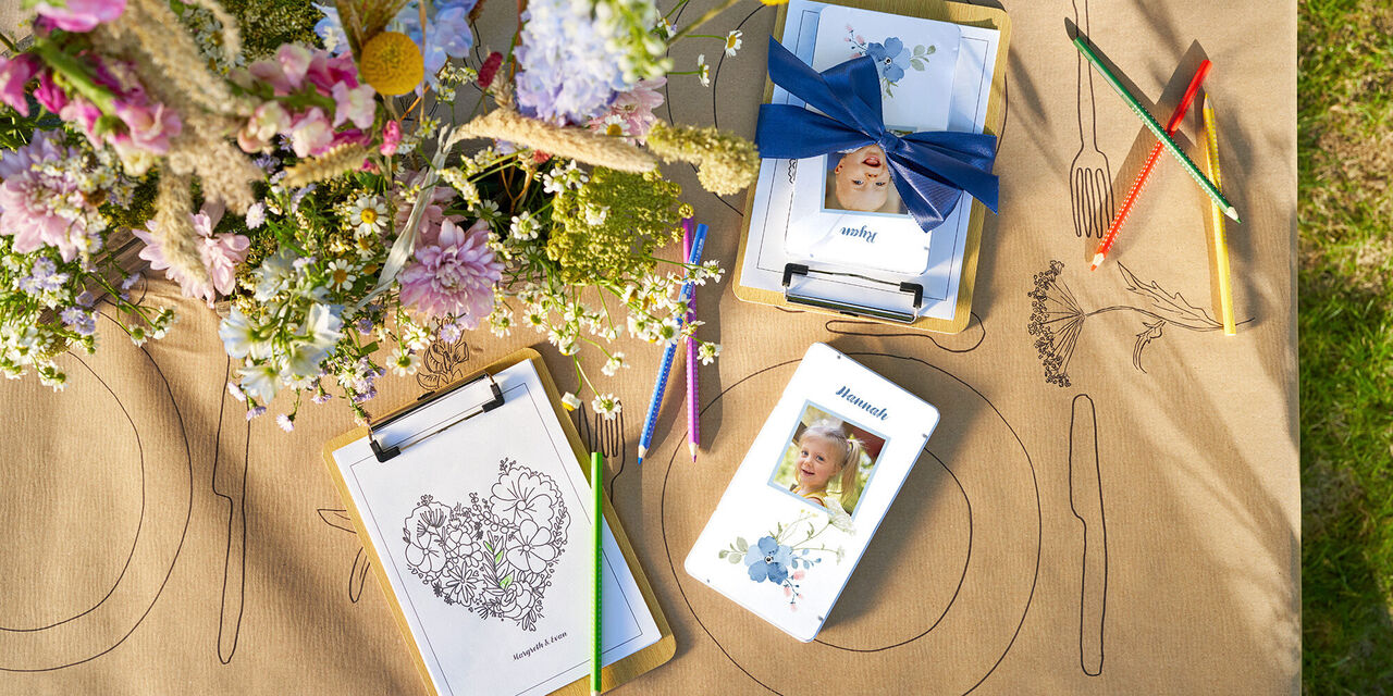 Na mizi so barvni svinčniki v kovinski škatli z otroško fotografijo in vzorcem cvetja ter motivom za barvanje.