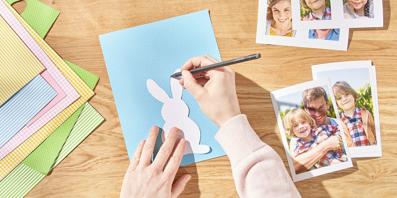 Dve roki narišeta velikonočnega zajčka na papir s pomočjo šablone. Zraven so natisnjene takojšnje fotografije družine.