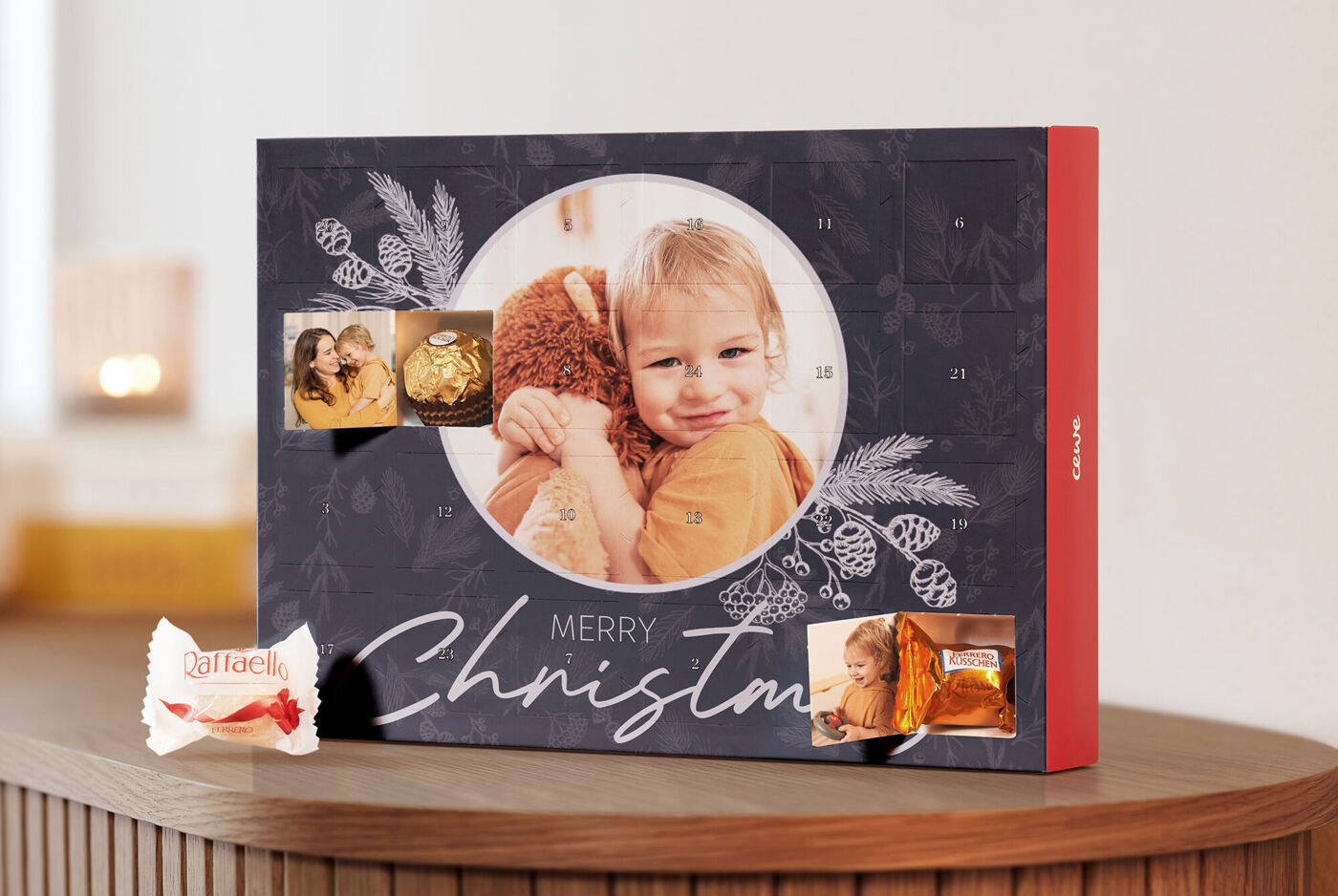 Praznični adventni koledar z veliko fotografijo in majhnimi slikami spredaj. Prikazani so božični motivi in napis 'MERRY CHRISTMAS'.